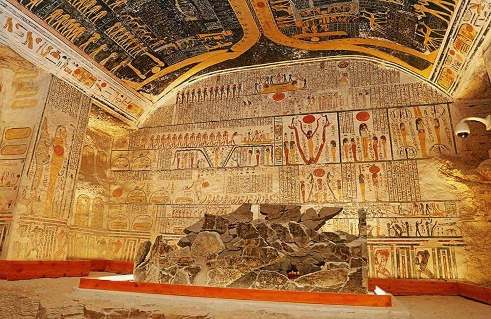 KV14 (Tomb of Tausret and Setnakhtt) featuring walls and ceilings filled with colorful funerary paintings, red solar discs, and hieroglyphics, centered around a damaged, dark stone sarcophagus base.